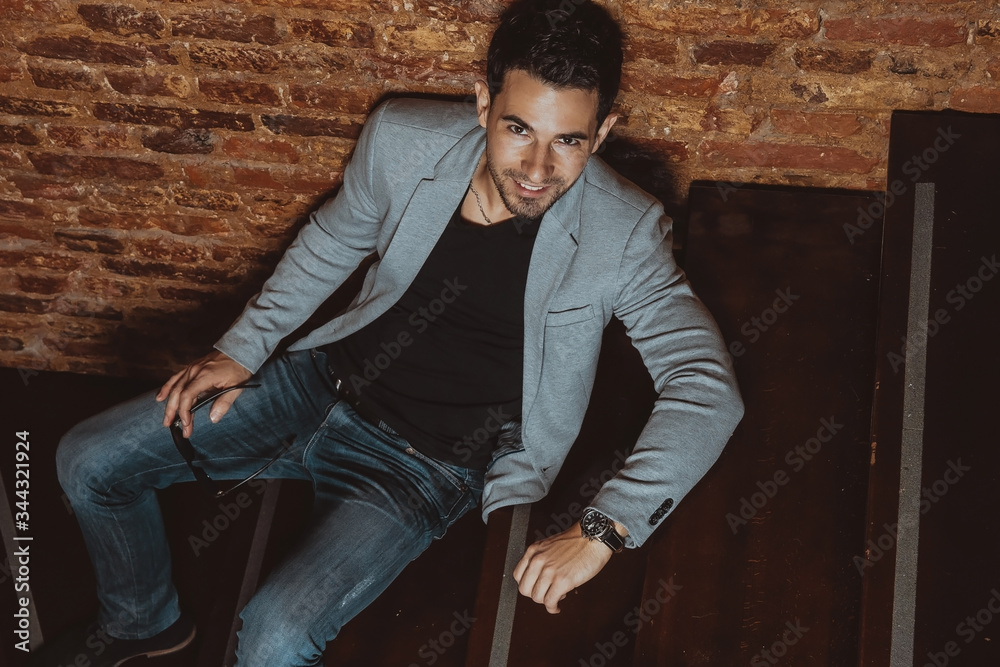 Portrait of a handsome stylish man posing in loft studio interior while lying on wooden stairs. Fashion for men. Portrait of a handsome stylish man posing in loft studio interior while lying on wooden stairs. Fashion for men.