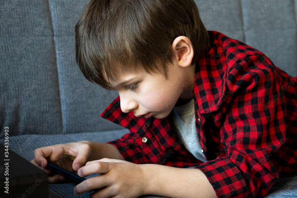 Focused boy enthusiastically plays in a smartphone. Leisure during self-isolation concept. Gadget dependence concept. Focused boy enthusiastically plays in a smartphone. Leisure during self-isolation concept. Gadget dependence concept.