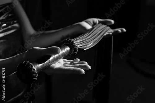 Close-up Black leather lash in female hands. Monochrome cropped photo of bdsms toys. A woman stands in the dark and holds a whip in her palms.