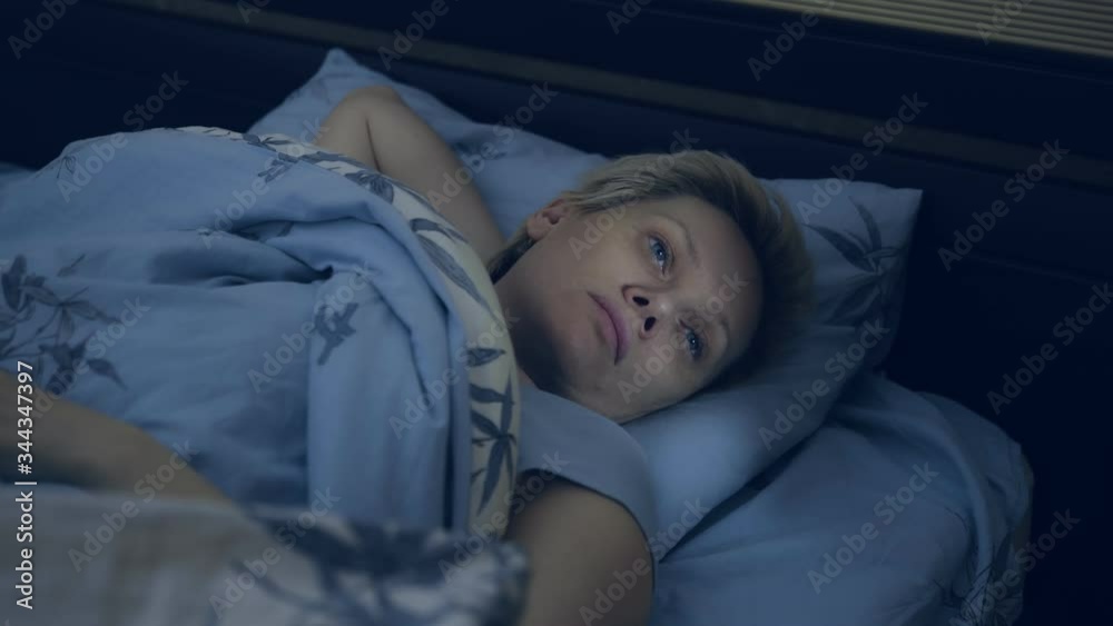 a woman suffering from insomnia lies in bed in the dark with her eyes open. a woman suffering from insomnia lies in bed in the dark with her eyes open.