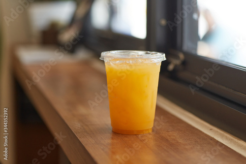 DISPOSABLE PLASTIC CUP DRINKS   plastic cup of tea for takeaway place on wood counter table in cafeteria  besides blur windows background. Close up and selective focus