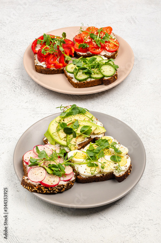 A variety of mini sandwiches with cream cheese and vegetables on plates, a light background.