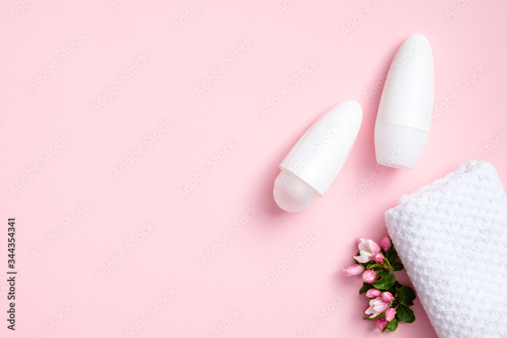 Deodorant antiperspirant bottles with flowers and towel on pink background. Flat lay, top view. Underarm skin care, sweat protection concept