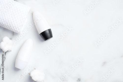 Roll-on deodorant bottles with cotton flowers and towel on marble background. Flat lay, top view. Underarm skin care, sweat protection concept
