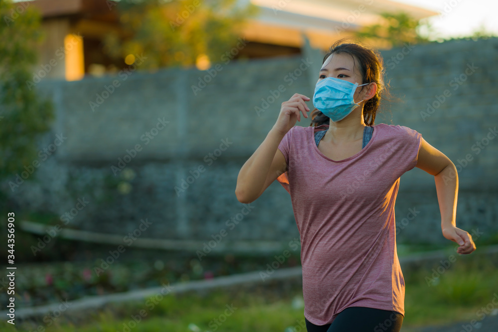 Naklejka premium Asian woman in anti pollution face mask running workout - young dedicated chinese girl jogging at beautiful city park on sunset enjoying fitness in covid-19 pandemic times