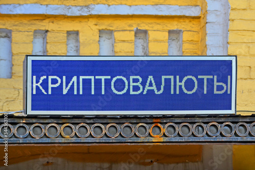Cryptocurrency, bitcoin, text on russian language on blue led display board on the yelllow brick wall, modern digital money mining,  crypto token exchange kiosk, currency monitor information diversity