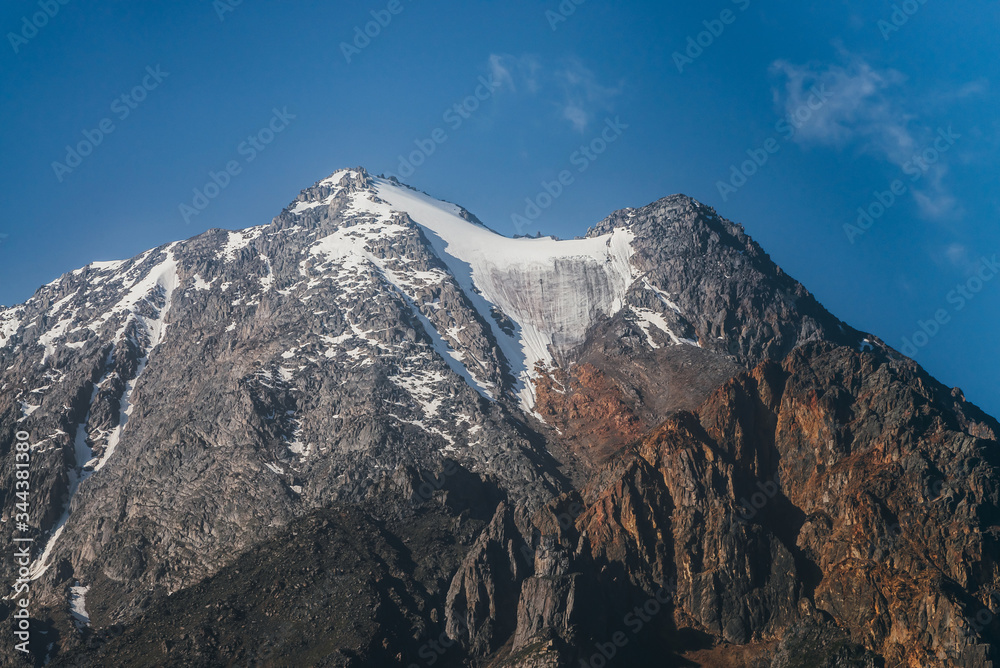 Awesome view to beautiful brown rock with snow in haze under clear blue sky. Minimal alpine landscape with big mountain with glacier. Atmospheric highland scenery with huge snowy rocky top in sunlight