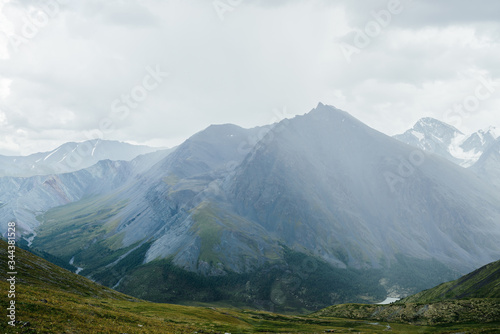 Atmospheric alpine view from pass to great mountain with sharp pinnacle under gloomy cloudy sky. Wonderful giant pointy rocky top and snowy mountains behind mountain pass. Awesome beauty of highlands.