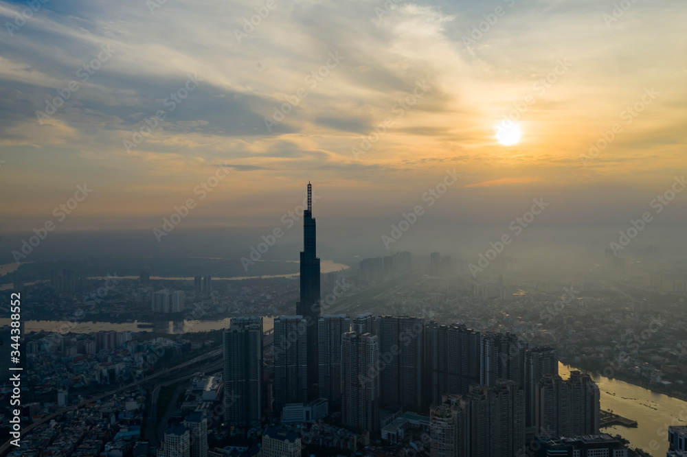 Sunrise drone shot of misty Ho Chi Minh City urban landcape with high rise tower in silhouette and view of river