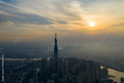 Sunrise drone shot of misty Ho Chi Minh City urban landcape with high rise tower in silhouette and view of river