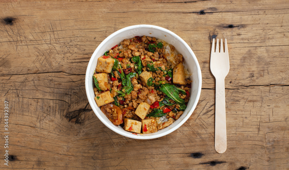 Thai basil pork stir fried with rice in food paper box on wooden table, takeaway street food, top view Thai basil pork stir fried with rice in food paper box on wooden table, takeaway street food, top view
