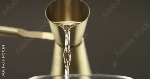 Close up of clear liquor pouring out of gold shot glass into a glass pitcher photo