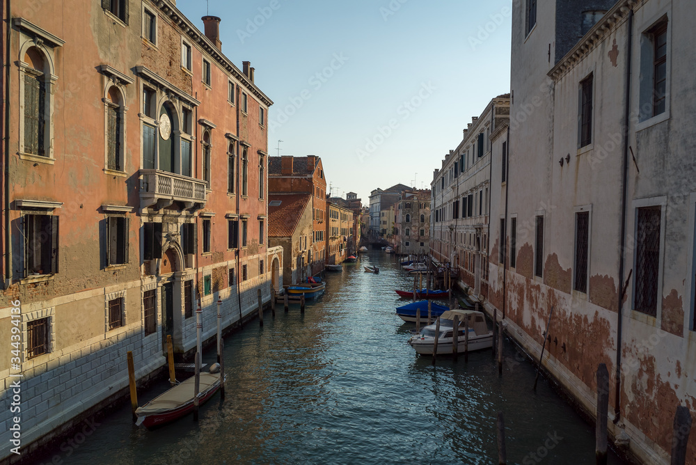 A scenic view of a beautiful Venetian canal on a warm sunny day with colourful houses and boats running along the water in the town of Venice, Italy