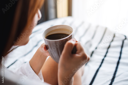 A beautiful woman drinking hot coffee in a white cozy bed at home in the morning