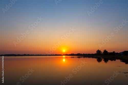 Landscape of the sunset over the tree and reflaction water in the canal at sisaket province , Thailand. The sun is falling on the horizon and reflecting water. photo