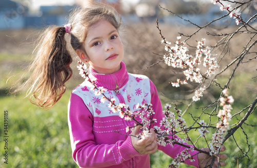 Girl near white flowers apricots on a branch. Spring portrait baby girl in the evening outdoors