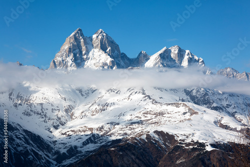 Majestic mount Ushba covered with snow, peeking above the clouds. Ushba is one of the most notable peaks of the Caucasus range, located in the Svaneti region of Georgia. Travel.