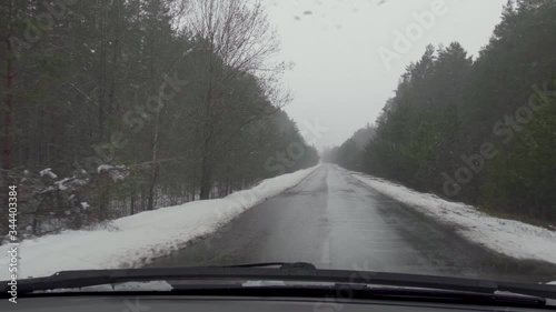 The car is driving on a road in the woods in a snowfall, the view from the car.