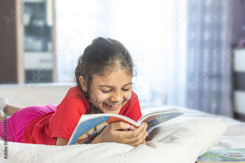 Beautiful girl reading book and smiling. Girl wearing red T-shirt, studying at home with books and doing school homework. Smiling girl. photo