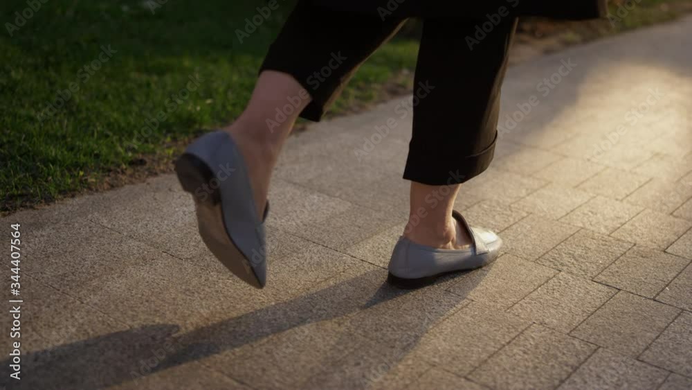 A girl in blue shoes is walking along the asphalt along the city sidewalk. Closeup of the legs of a woman running in black trousers. Background close-up. Female legs on the road in sports shoes. A girl in blue shoes is walking along the asphalt along the city sidewalk. Closeup of the legs of a woman running in black trousers. Background close-up. Female legs on the road in sports shoes.