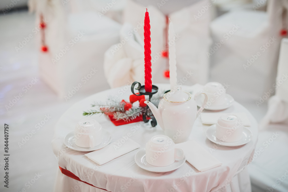 Romantic gala dinner setting with red and white candles on white tablecloth and napkins. Romantic white tea table with candles. Romantic gala dinner setting with red and white candles on white tablecloth and napkins. Romantic white tea table with candles.