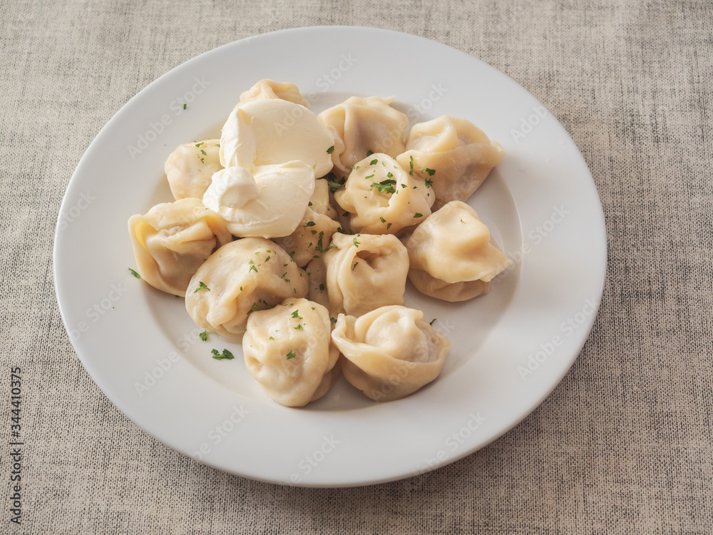 Portion of dumplings on a white plate with sour cream.