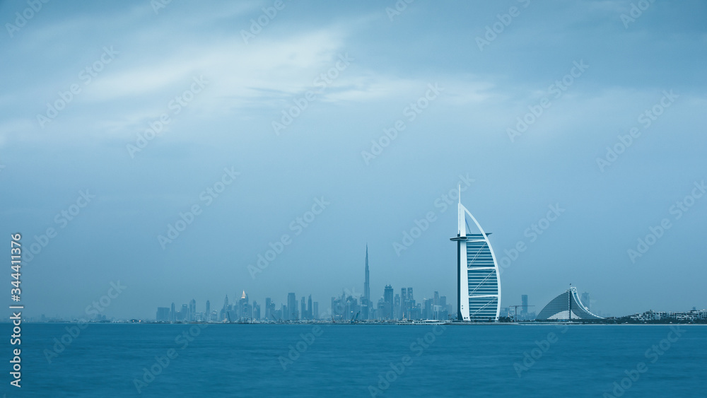 Fototapeta premium Viewing Dubai cityscape with Jumeirah coast and Downtown across the sea on a moody cloudy day. Dubai, United Arab Emirates.