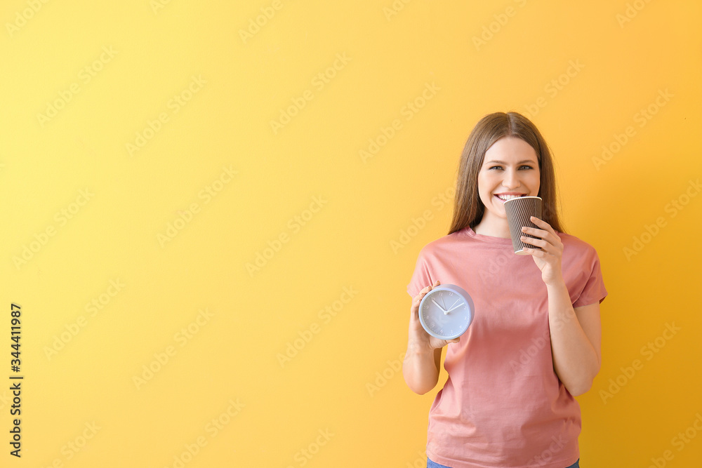 Young woman with alarm clock drinking coffee on color background Young woman with alarm clock drinking coffee on color background
