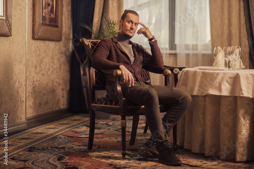 A young businessman in casual clothes, sitting in a luxury apartment and thinking, making an important decision.