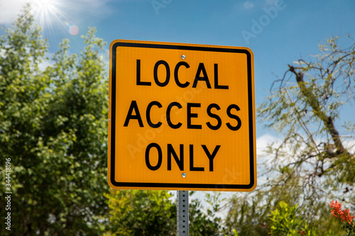 Yellow and black square road sign in neighborhood reading Local Access Only agasint a blue sky with palm trees