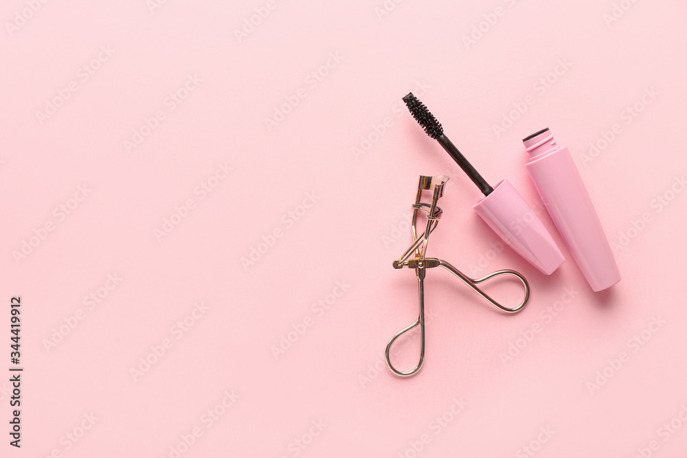 Mascara and eyelash curler on color background