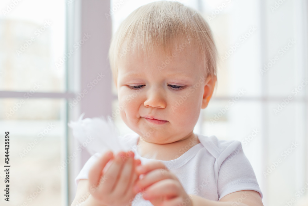 A small Caucasian girl sits alone on the windowsill and plays with white feathers.