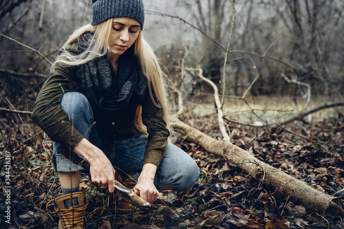 Woman tourist cuts wooden stick with knife in forest. Bushcraft Survival and Scouting Concept photo