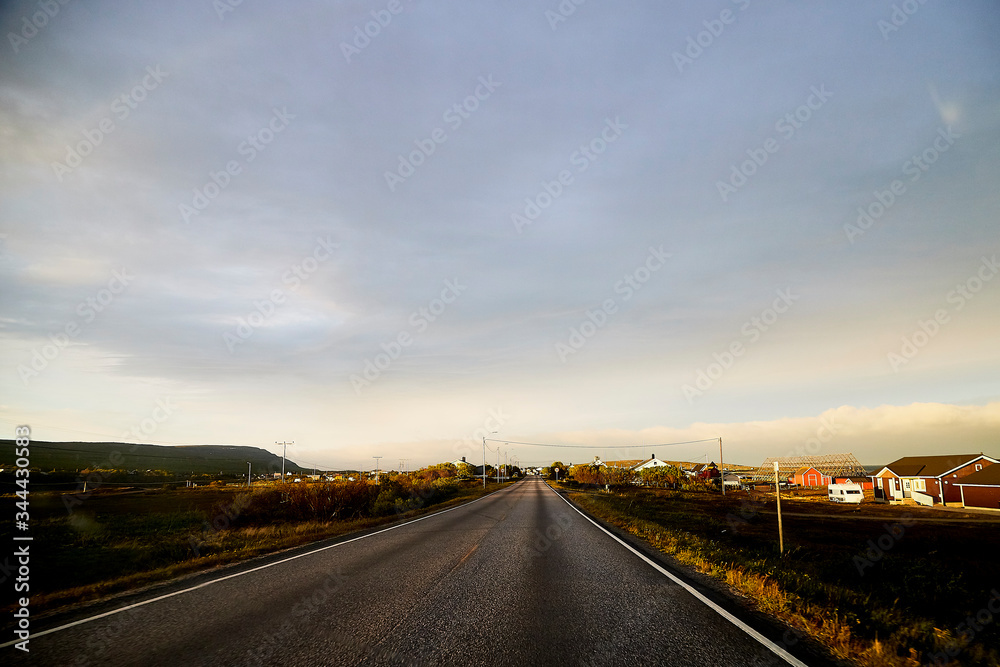 Fototapeta premium View on the road and interesting landscape with tundra, village and cloudy sky. Landscape in Norway
