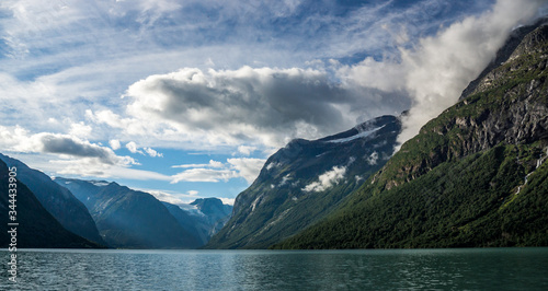 fjord and river in norway during summer with mountains and cloudy blue sky