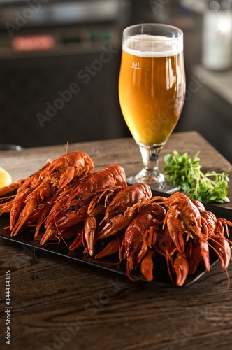 Plate with boiled crayfish and glass of light beer are on a bar counter. Vertical poster