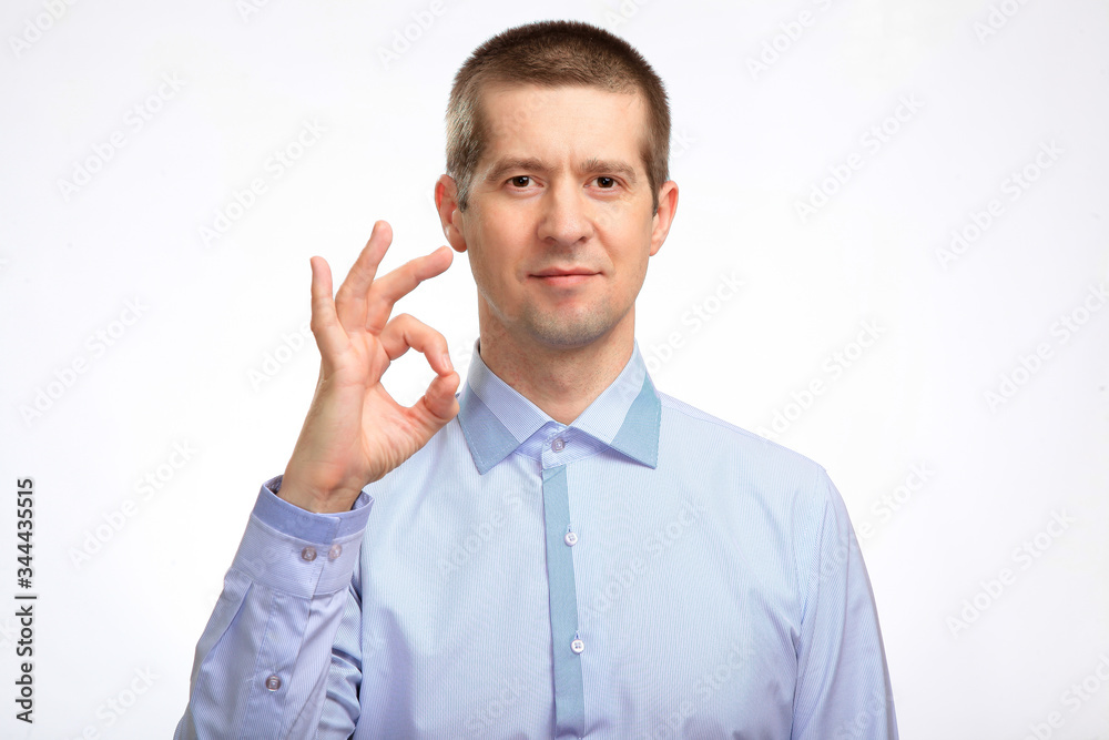 successful happy man shows the gesture OK with one hand, in a blue light casual shirt staring at the camera. Isolated successful happy man shows the gesture OK with one hand, in a blue light casual shirt staring at the camera. Isolated