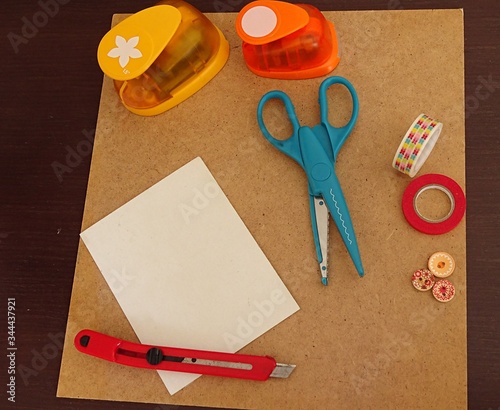 scrapbook material: scissors, machine to make holes with shapes, buttons, paper, adhesive tape