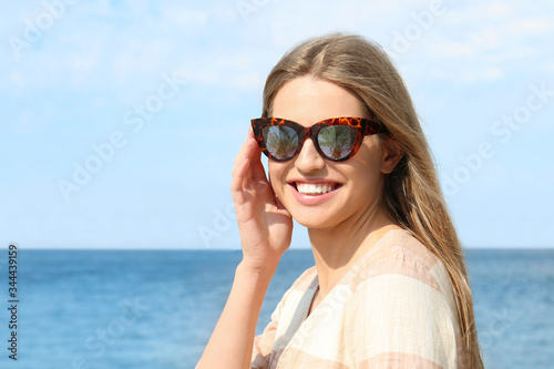 Young woman wearing stylish sunglasses with reflection of palm trees near sea
