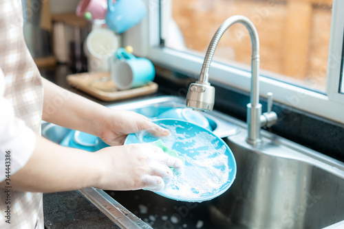 Close up hand of attractive young Asian woman is washing dishes at kitchen sink while doing cleaning at home during Staying at home using free time about their daily housekeeping routine..
