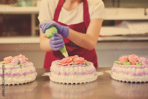 The process of decorating cakes in a pastry shop. A pastry chef makes flowers out of cream.