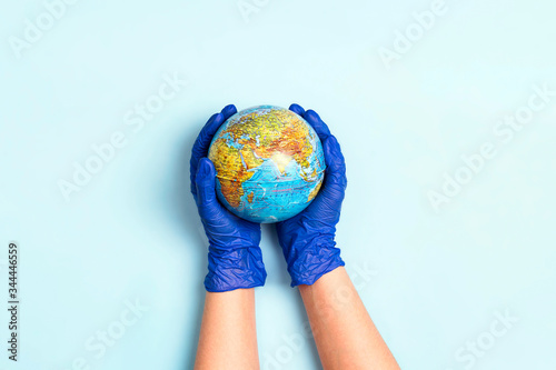 Hands in medical gloves holding a globe on blue background.