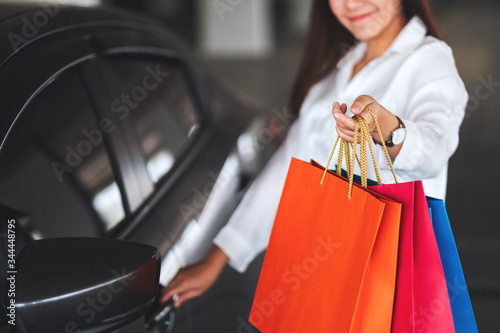 Closeup image of a beautiful woman holding and showing shopping bags while opening car door in the mall parking lot