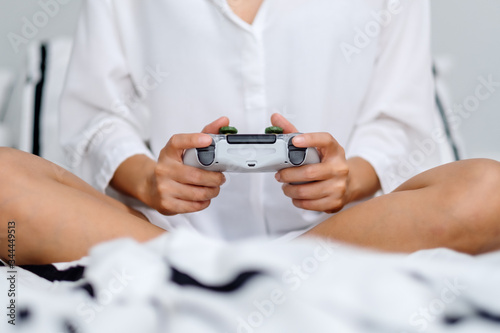 Closeup image of a woman holding game controller while playing games   sitting on a white cozy bed at home