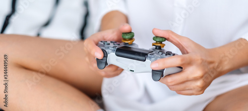 Closeup image of a woman holding game controller while playing games , sitting on a white cozy bed at home