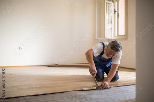 DIY, repair, building and home concept - close up of male hands lying parquet floor board/laminate flooring (shallow DOF; color toned image)