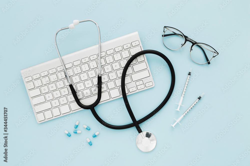 Stethoscope and keyboard on medical desk top view blue
