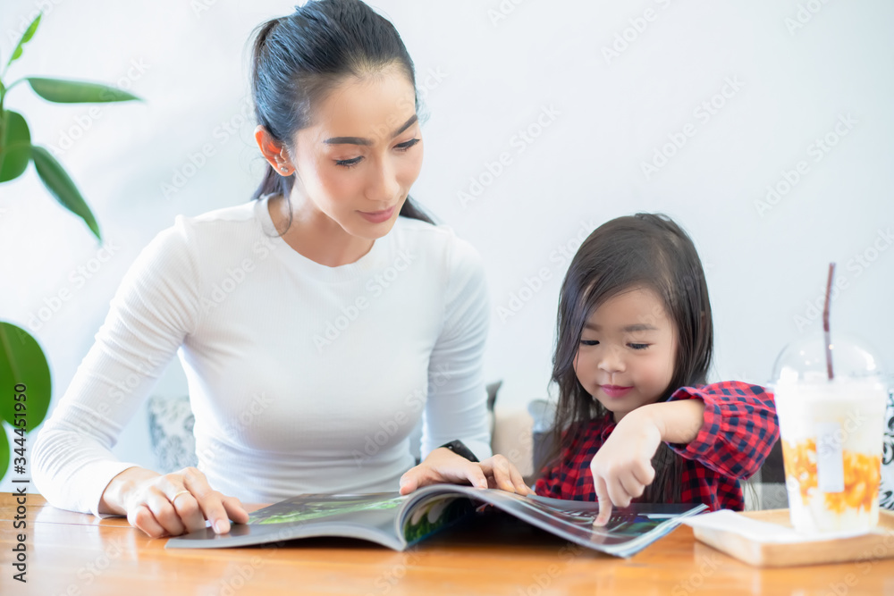 An Asian mother is teaching her daughter to read a book during the semester break on the living table and having cold milk on the table at home. Educational concepts and activities of the family An Asian mother is teaching her daughter to read a book during the semester break on the living table and having cold milk on the table at home. Educational concepts and activities of the family