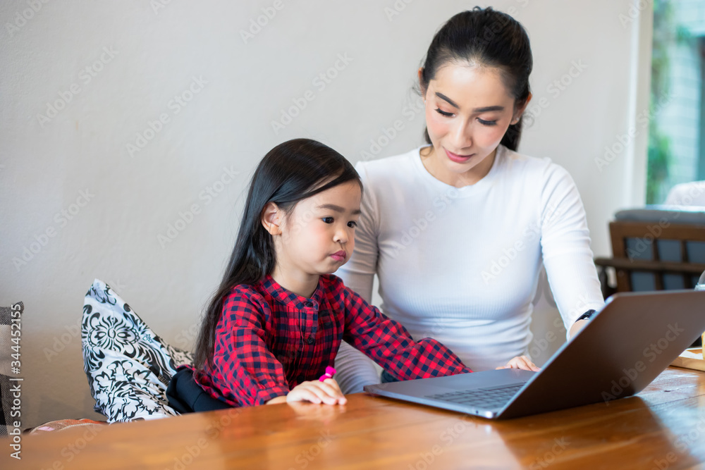 Asian mothers are teaching their daughters to read a book and use notebooks and technology for online learning during school holidays at home. Educational concepts and activities of the family Asian mothers are teaching their daughters to read a book and use notebooks and technology for online learning during school holidays at home. Educational concepts and activities of the family