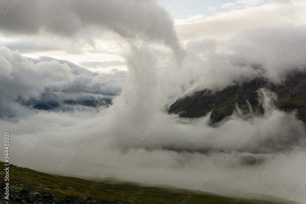 Morning mist is rising towards the peaks of the Laddjuvaggi valley slopes in Sweden Lapland